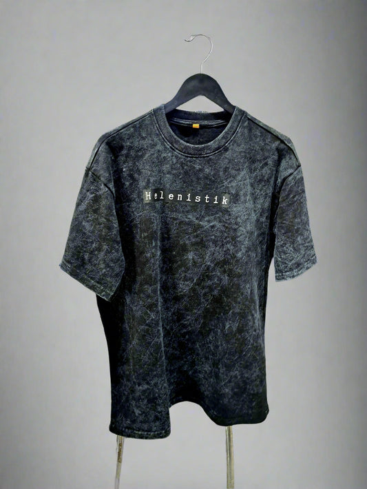Black acid-wash t-shirt with 'Hellenistic' text on a hanger in a store setting.